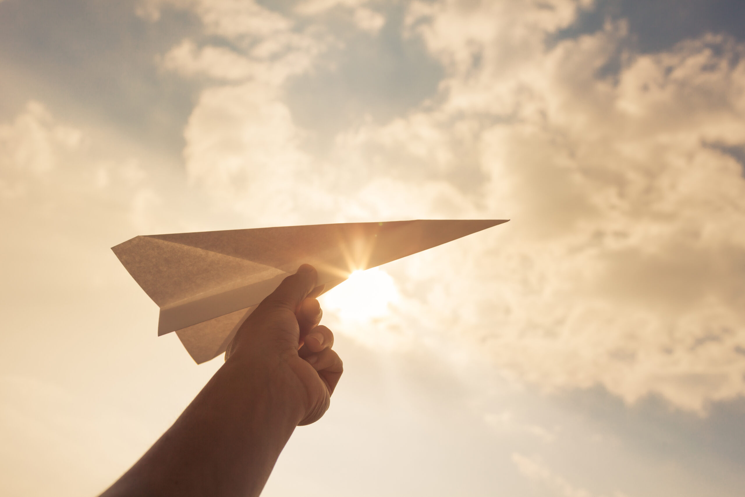 Taking flight! hand holding paper airplane in the sky.
